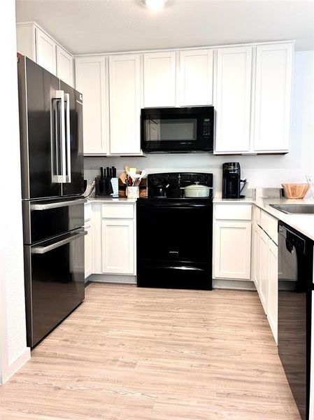 Kitchen with black appliances, white cabinets, light countertops, and light wood-style flooring Kitchen with black appliances, white cabinets, light countertops, and light wood-style flooring