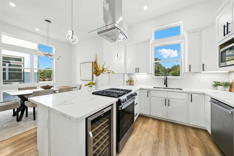 Modern chef-inspired kitchen with clean white finishes and abundant natural light, featuring Quartz countertops, a large waterfall island, custom soft-close cabinetry, and a stylish herringbone tile backsplash. Equipped with a gas cooktop, stainless steel vent hood, built-in microwave, wine fridge, and sleek black fixtures, this open-concept kitchen flows seamlessly into the dining area Modern chef-inspired kitchen with clean white finishes and abundant natural light, featuring Quartz countertops, a large waterfall island, custom soft-close cabinetry, and a stylish herringbone tile backsplash. Equipped with a gas cooktop, stainless steel vent hood, built-in microwave, wine fridge, and sleek black fixtures, this open-concept kitchen flows seamlessly into the dining area