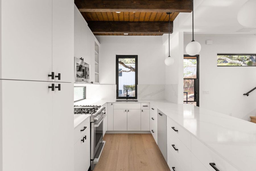 Kitchen featuring stainless steel appliances, white cabinetry, hanging light fixtures, light wood-style flooring, and a wooden ceiling with exposed beams
