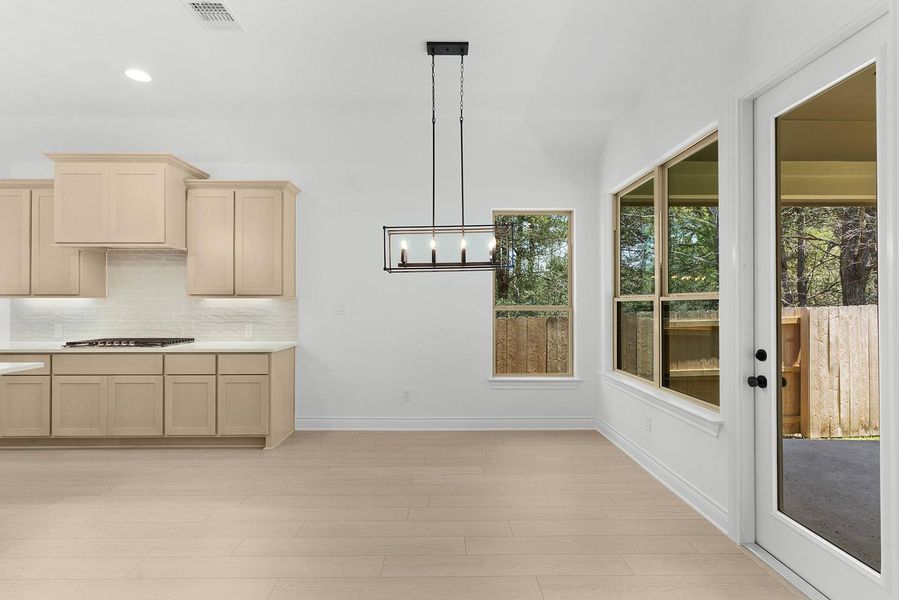 A well-lit dining area connects seamlessly to a modern kitchen, featuring a striking chandelier and backyard access.