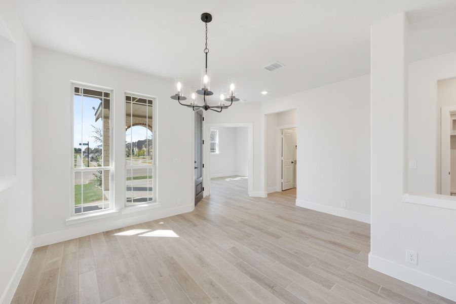 Empty dining room with light wood floors, white walls, and a black chandelier overhead
