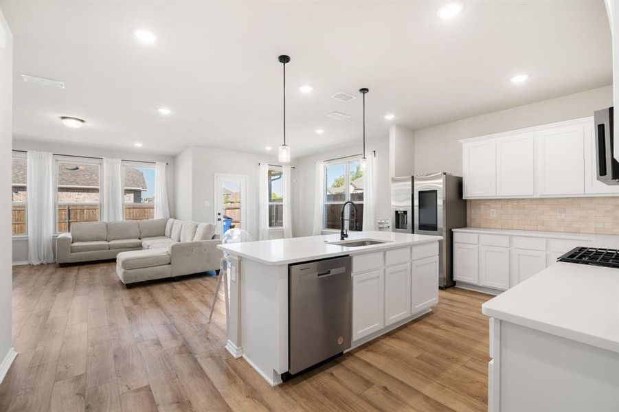 Kitchen with backsplash, white cabinetry, decorative light fixtures, a kitchen island with sink, and stainless steel appliances Kitchen with backsplash, white cabinetry, decorative light fixtures, a kitchen island with sink, and stainless steel appliances