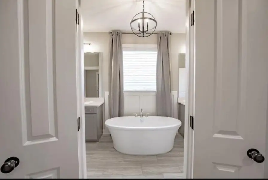 Freestanding soaking tub with a floor-mounted faucet, wood-finish flooring, white window blinds, board and batten wall paneling, and an orb chandelier