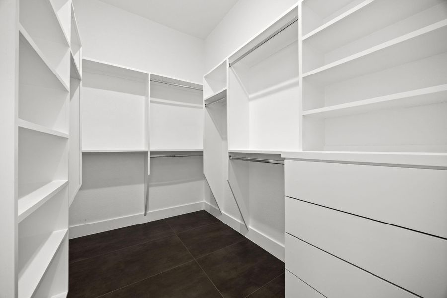 Spacious walk-in closet with ample shelving, hanging space, and modern dark flooring, perfect for organized storage.