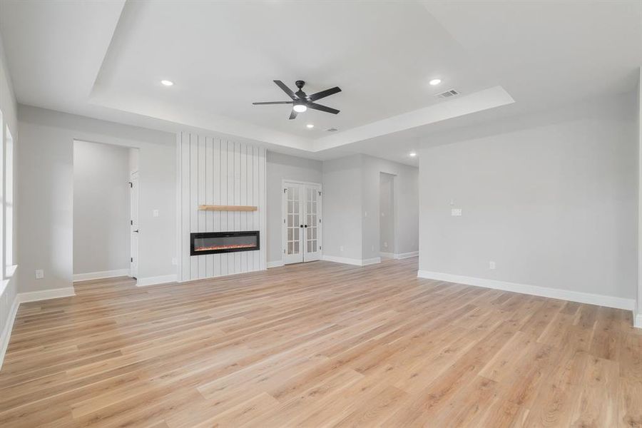 Unfurnished living room with ceiling fan, a raised ceiling, light hardwood / wood-style flooring, and a large fireplace