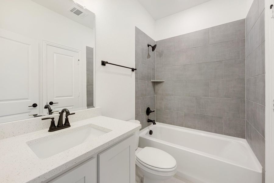 Bathroom with white quartz vanity, toilet, and tub-shower combo with gray tile surround and black fixtures Bathroom with white quartz vanity, toilet, and tub-shower combo with gray tile surround and black fixtures