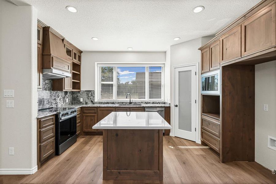 Kitchen with stainless steel appliances, light wood-style floors, a textured ceiling, tasteful backsplash, and open shelves