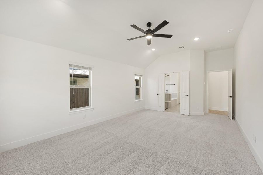 Empty bedroom with vaulted ceiling, ceiling fan, carpet flooring, and doors leading to ensuite bathroom