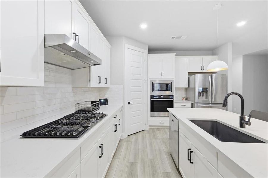 Kitchen featuring white cabinets, pendant lighting, tasteful backsplash, stainless steel appliances, and under cabinet range hood