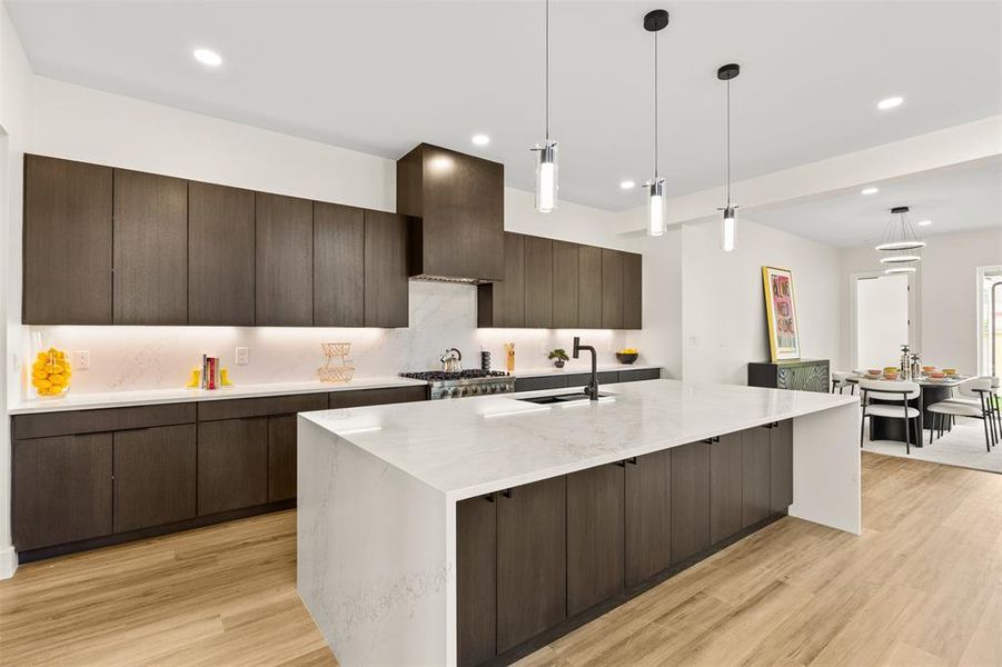 Modern kitchen featuring a large center island with a white countertop, dark wood-finish cabinetry, integrated stainless steel appliances, and wood-finish flooring