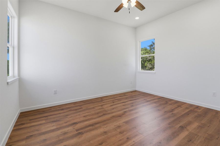 Bright room featuring wood-finish flooring, white walls, and a ceiling fan with light fixture Bright room featuring wood-finish flooring, white walls, and a ceiling fan with light fixture