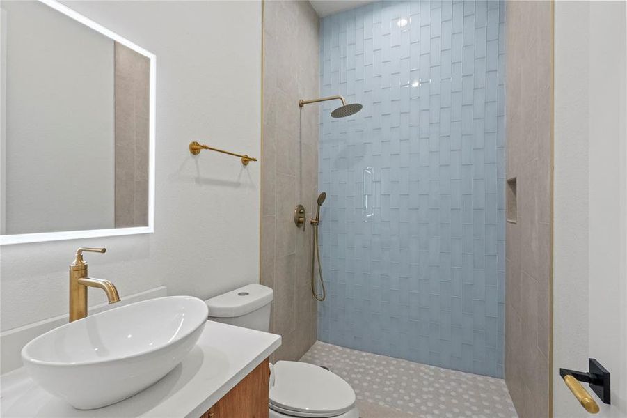 Bathroom featuring tiled shower, toilet, and vanity