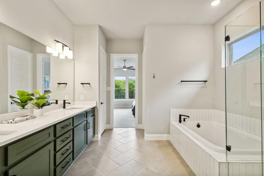 Bathroom with tile patterned floors, ceiling fan, tiled tub, and vanity