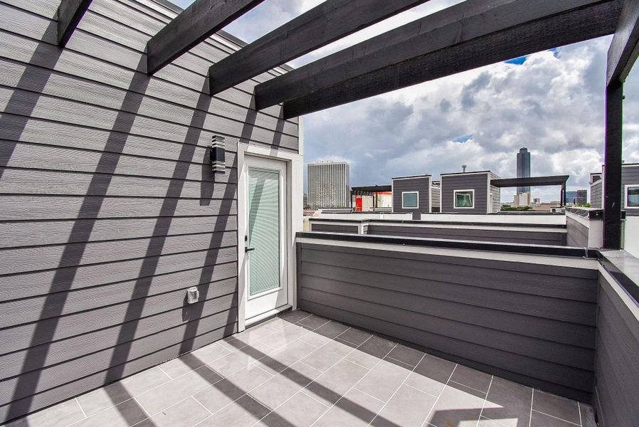 Modern rooftop terrace with sleek gray siding and a pergola, offering city skyline views. Ideal for outdoor relaxation and entertaining.