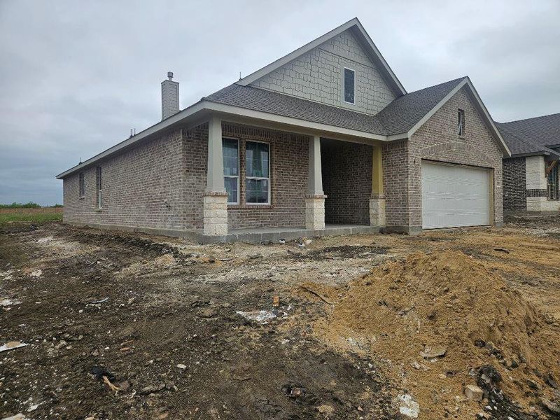New construction exterior featuring a brick facade with stone accents, a covered front porch, a two-car garage, and a gabled roofline with shingle siding New construction exterior featuring a brick facade with stone accents, a covered front porch, a two-car garage, and a gabled roofline with shingle siding
