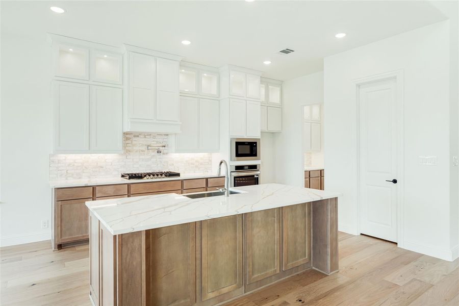 Kitchen with large center island, white upper cabinets, wood lower cabinets, quartz countertops, and stainless steel appliances