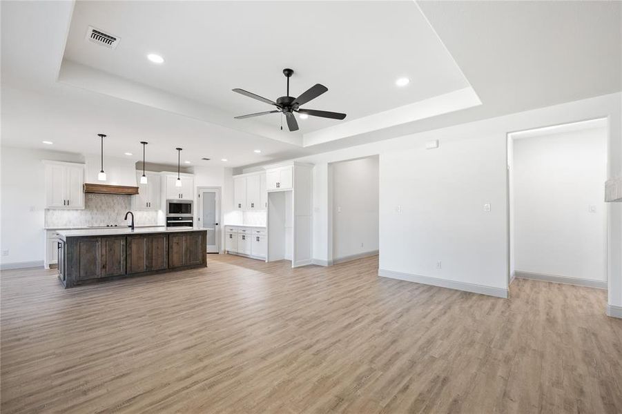 Unfurnished living room featuring a raised ceiling, light wood finished floors, recessed lighting, and a ceiling fan