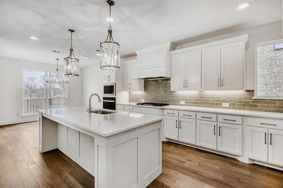 Kitchen featuring white cabinetry, decorative light fixtures, light stone countertops, and a center island with sink