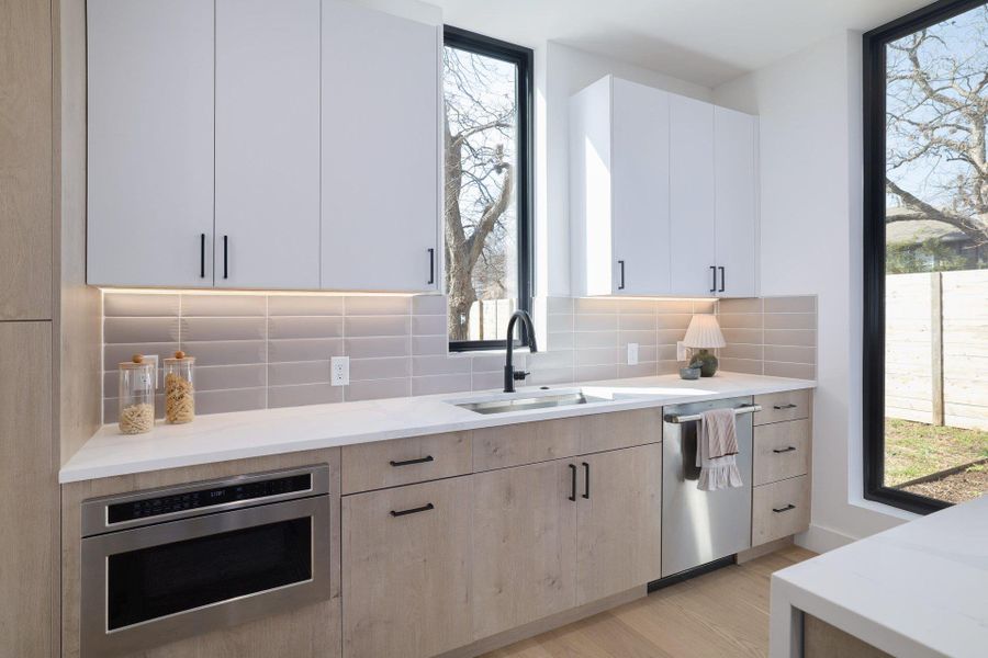 Kitchen with light stone countertops, stainless steel appliances, tasteful backsplash, light wood-type flooring, and modern cabinets