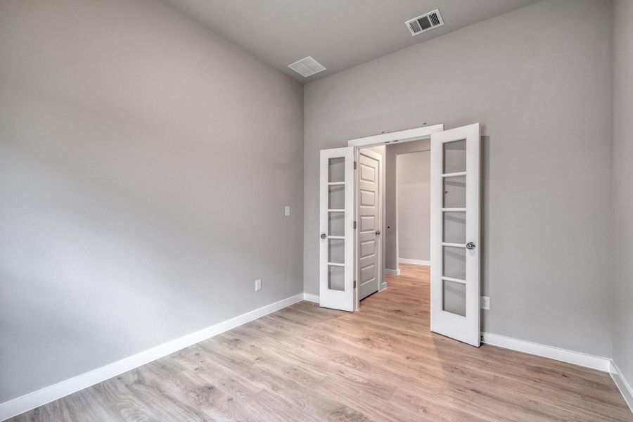 French doors open into a versatile room with light wood flooring and neutral walls. French doors open into a versatile room with light wood flooring and neutral walls.