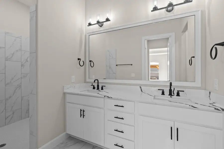 Retreat to the Portico’s spa-inspired primary bath, featuring a walk-in shower, dual vanities, and timeless finishes designed for comfort and style. Image depicts home as-is.