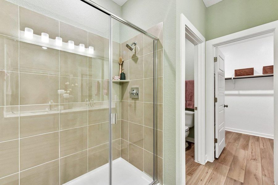 Tiled walk-in shower stands adjacent to a functional walk-in closet with wood-look flooring. Tiled walk-in shower stands adjacent to a functional walk-in closet with wood-look flooring.