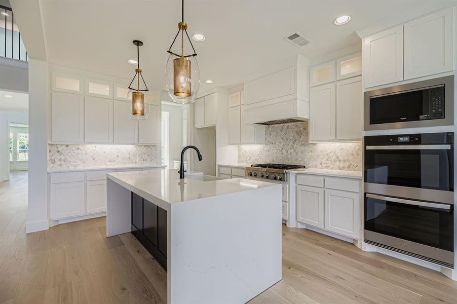 Kitchen featuring appliances with stainless steel finishes, light countertops, recessed lighting, light wood-style flooring, and glass insert cabinets