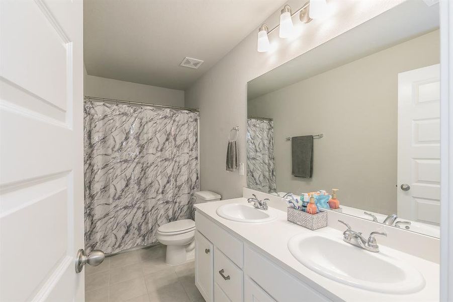 Bathroom with double vanity, light tile patterned floors, and curtained shower