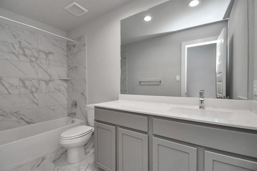 Secondary bath features tile flooring, bath/shower combo with tile surround, light stained wood cabinets, beautiful light countertop.