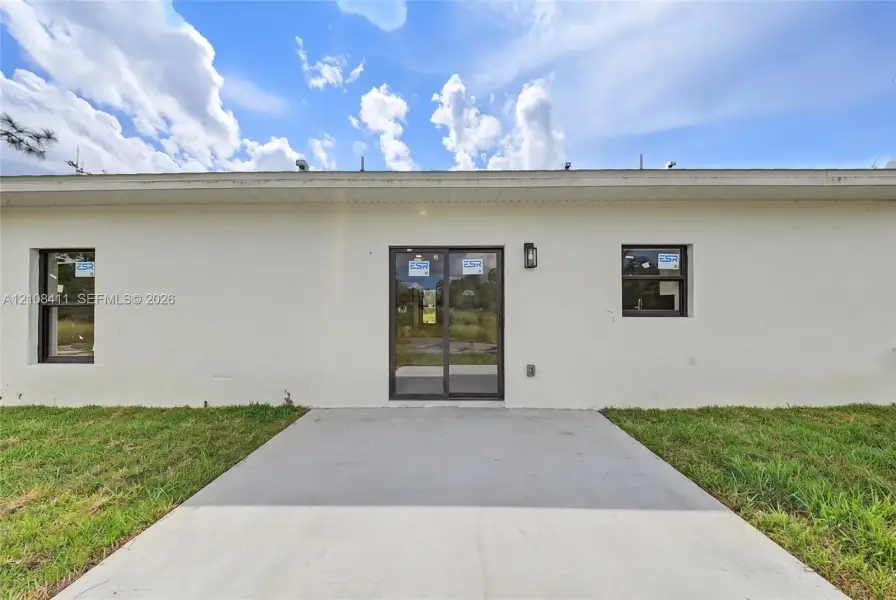 Stucco exterior finish, concrete patio, sliding glass door, and two single-pane windows with dark frames