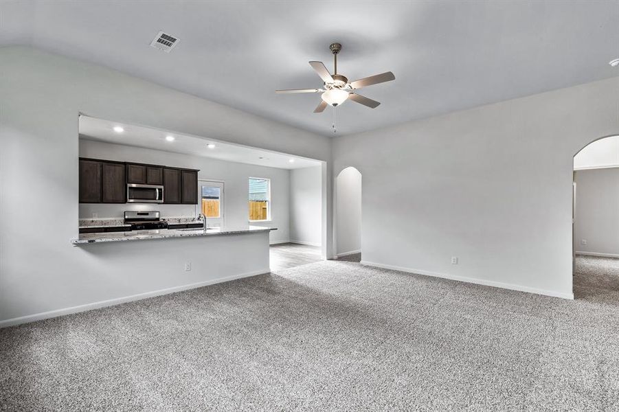 Unfurnished living room with sink, light carpet, ceiling fan, and lofted ceiling