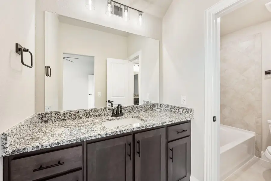 Bathroom with dark wood vanity, granite countertop, large mirror, and tiled soaking tub area