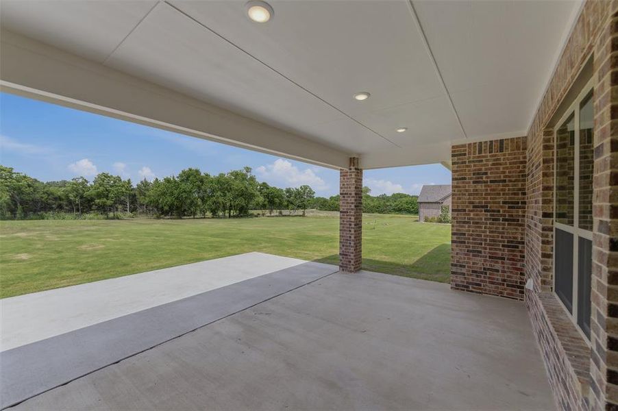 Expansive covered patio featuring a concrete surface, brick support columns, and recessed lighting Expansive covered patio featuring a concrete surface, brick support columns, and recessed lighting