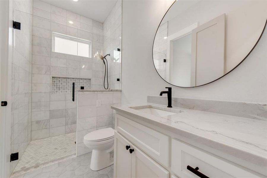 Bathroom featuring tile flooring, a tile shower, tile walls, vanity, and toilet