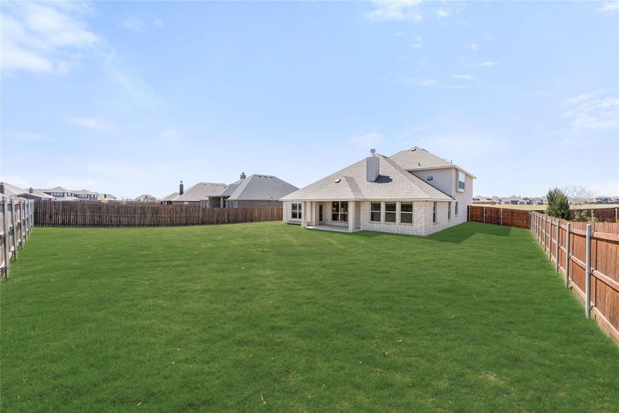 Brick home rear view with large fenced backyard, covered patio, and green lawn