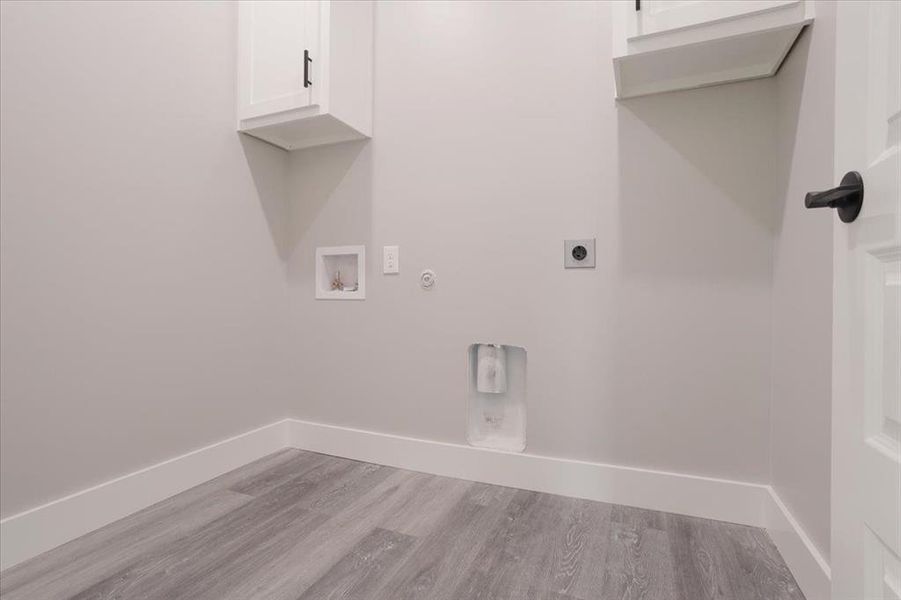 Clothes washing area featuring hookup for a washing machine, electric dryer hookup, light hardwood / wood-style floors, and cabinets