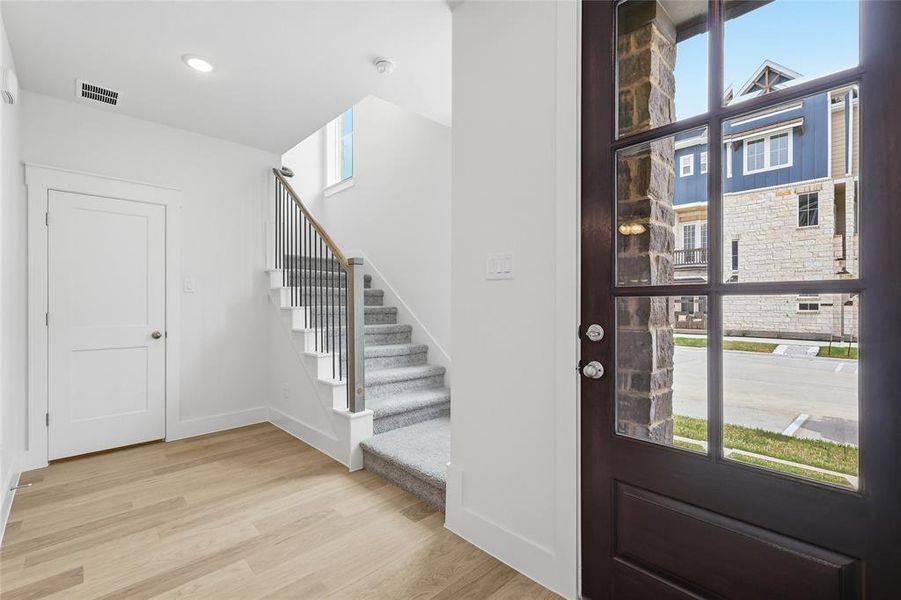 The property features light-toned flooring, a carpeted staircase with a metal and wood railing, and a white interior door