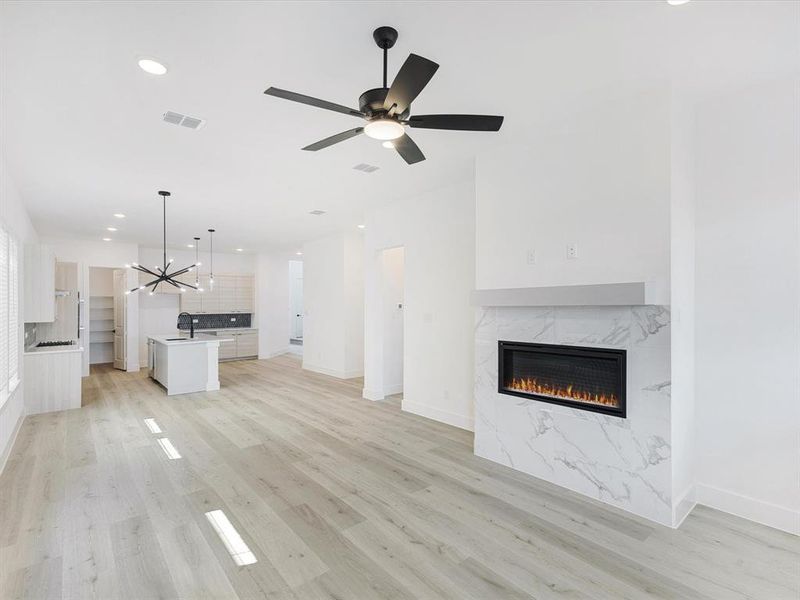 Unfurnished living room with recessed lighting, light wood-style flooring, a high end fireplace, a chandelier, and ceiling fan Unfurnished living room with recessed lighting, light wood-style flooring, a high end fireplace, a chandelier, and ceiling fan