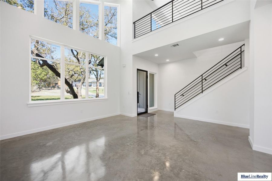 Unfurnished living room featuring finished concrete flooring, a high ceiling, and recessed lighting