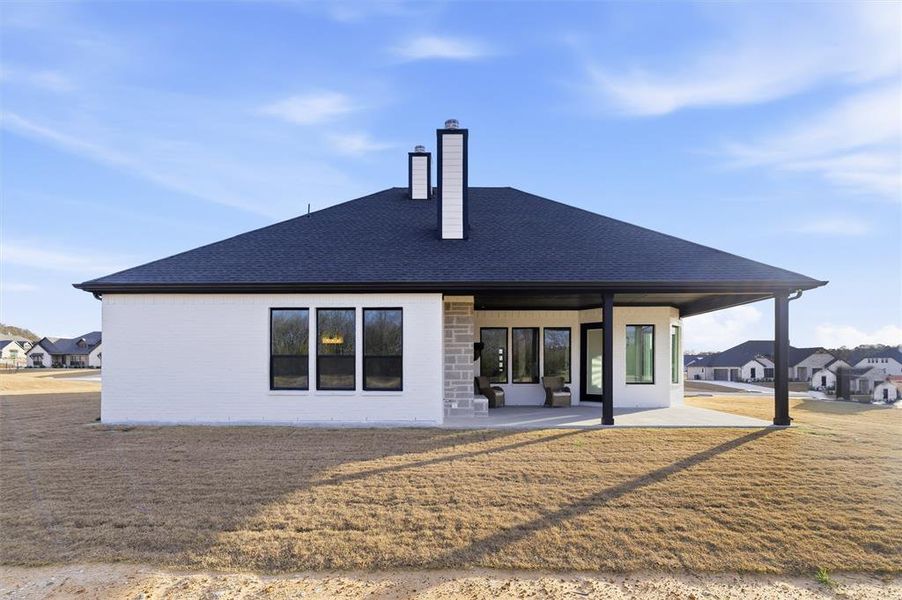 Rear view of house with a chimney, a patio, roof with shingles, a lawn, and brick siding