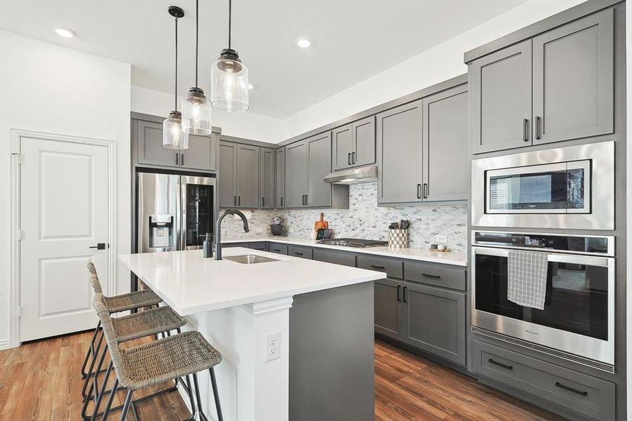 Kitchen with gray cabinets, appliances with stainless steel finishes, decorative backsplash, hardwood / wood-style flooring, and sink