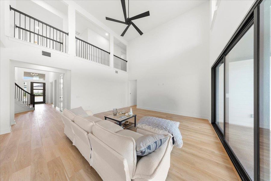 Living room with light wood finished floors, a towering ceiling, stairway, and a ceiling fan Living room with light wood finished floors, a towering ceiling, stairway, and a ceiling fan