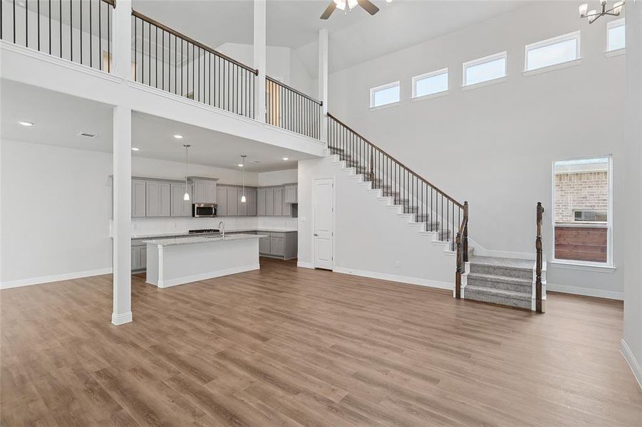 Unfurnished living room with light wood finished floors, a high ceiling, healthy amount of natural light, a ceiling fan, and recessed lighting Unfurnished living room with light wood finished floors, a high ceiling, healthy amount of natural light, a ceiling fan, and recessed lighting