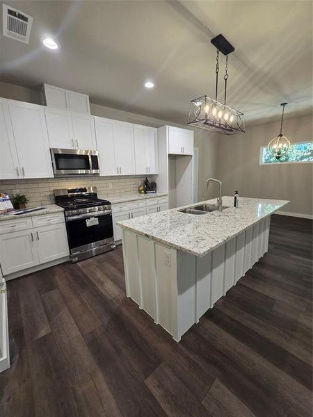 Kitchen featuring an island with sink, white cabinets, sink, and range