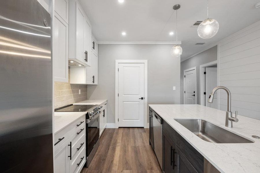 Two tone kitchen with stainless steel appliances, light stone counters, pendant lighting, dual tone cabinets, and backsplash