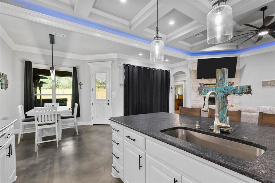 Kitchen with sink, ceiling fan, coffered ceiling, white cabinets, and crown molding