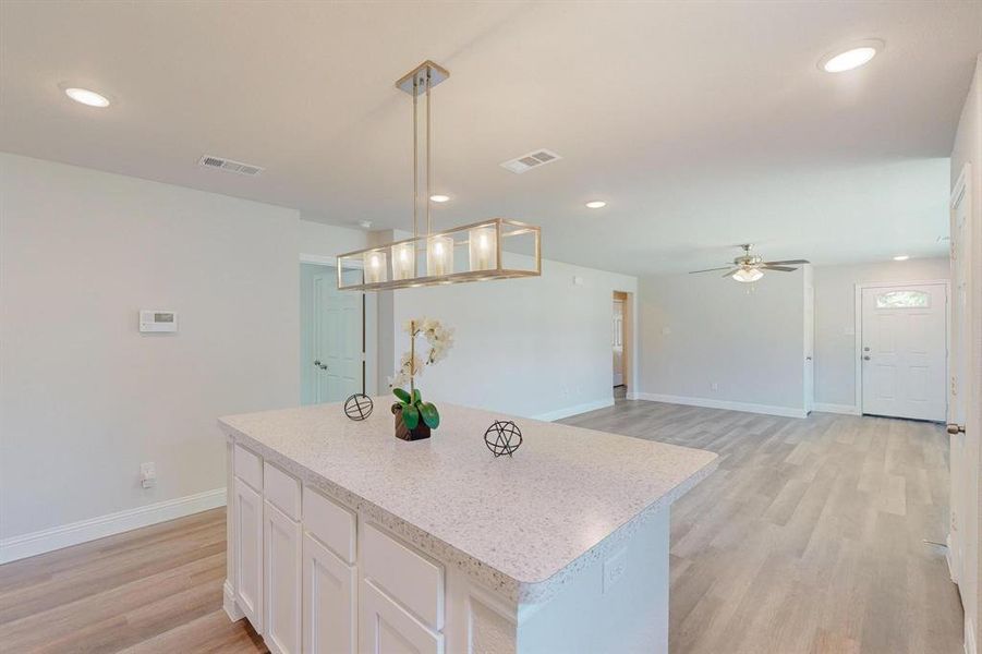 Kitchen with ceiling fan, white cabinets, a kitchen island, decorative light fixtures, and light hardwood / wood-style flooring