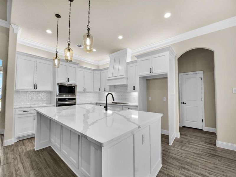 Kitchen featuring light stone countertops, stainless steel appliances, pendant lighting, a center island with sink, and white cabinetry