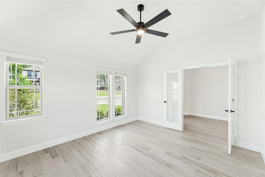 Empty bedroom with vaulted ceiling, black ceiling fan, light wood floors, and French doors