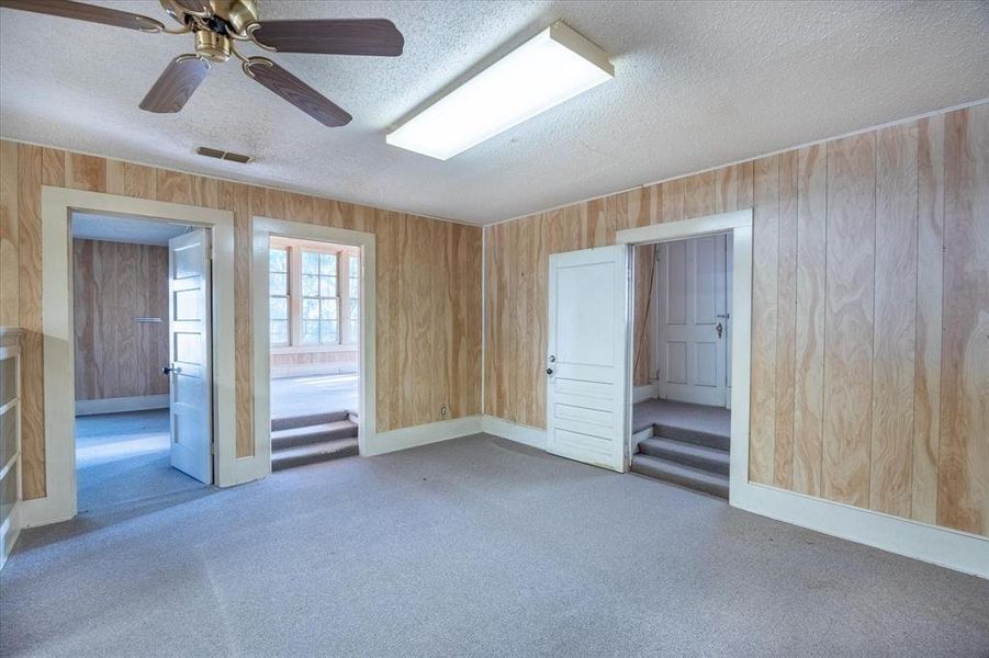 Carpeted empty room with ceiling fan, wood walls, and a textured ceiling